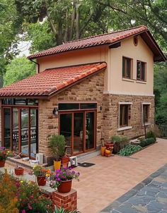 a small house with lots of plants and flowers in the front yard, surrounded by trees