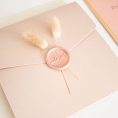 a pink envelope with a button and some feathers on it