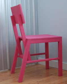 a pink chair sitting on top of a hard wood floor next to a white wall