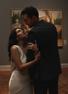 a man and woman standing next to each other in front of a painting on the wall