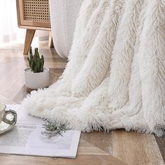 a white blanket sitting on top of a wooden floor next to a potted plant