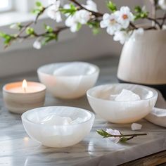 three white bowls sitting on top of a table next to a vase filled with flowers