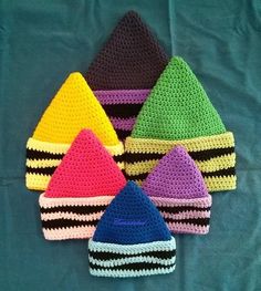 six crocheted hats are arranged on a blue surface, one is multicolored