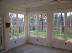 an empty room with three windows and a ceiling fan in the corner, looking out onto a grassy field