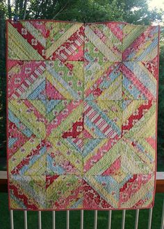 a colorful quilt hanging on the side of a wooden fence in front of some trees