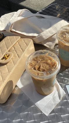 two cups of iced coffee sitting on top of a table next to a purse and cell phone