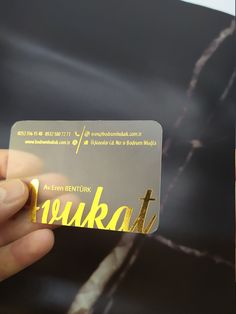 a person holding up a business card with gold lettering