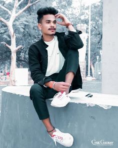 a man sitting on top of a cement wall wearing white shoes and a black jacket