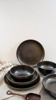 a table topped with black plates and spoons on top of a white cloth covered table