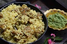 a pan filled with rice and meat next to a bowl of green sauce