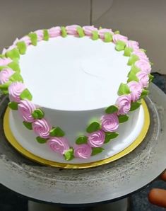 a white cake with pink and green frosting on a silver platter next to a person's hand