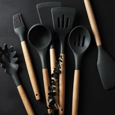 five kitchen utensils lined up in a row on a black surface with wooden handles