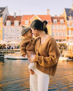 a woman holding a small child in her arms while standing next to a body of water