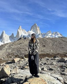 a woman standing on top of a rock covered field next to snow capped mountain peaks