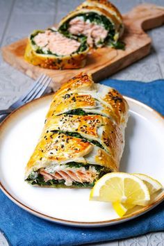 a white plate topped with a roll covered in meat and veggies next to a slice of lemon