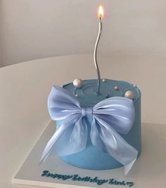 a blue birthday cake with a white bow on it and a candle in the middle