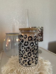 a glass candle holder sitting on top of a white table next to a silver vase