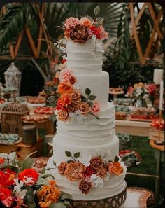 a white wedding cake with flowers on top and greenery in the backgroun