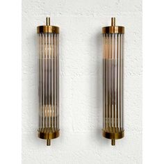 two brass and glass wall sconces on a white brick wall, one has a light bulb in the middle