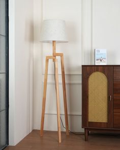 a wooden floor lamp next to a cabinet with a radio on it and a poster