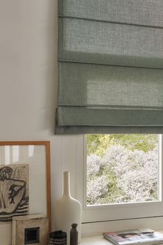 a window with a green roman blind in front of it and pictures on the side