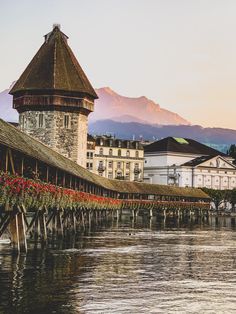 an old building is next to the water with flowers growing on it and mountains in the background