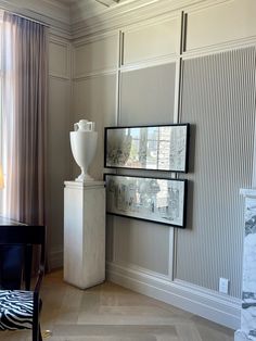 a white vase sitting on top of a table next to a wall mounted art piece