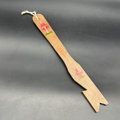 a wooden toothbrush with an arrow shaped handle on a gray surface and pink flowers