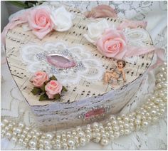 a heart shaped box sitting on top of a table next to pearls and pink roses