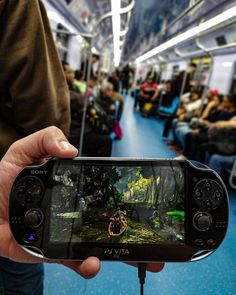 a person holding up a video game controller in front of the camera on a train