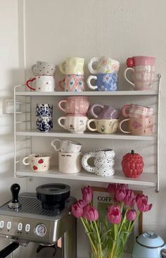 a shelf filled with cups and mugs next to a toaster on top of a stove