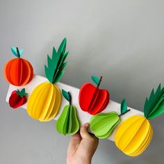 a person holding up some paper fruit on a long piece of white paper with green leaves and oranges