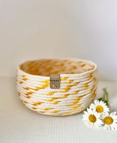 a yellow and white basket sitting on top of a table next to some daisies