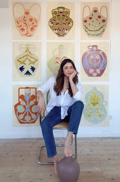 a woman is sitting on a chair in front of some art and posing for the camera