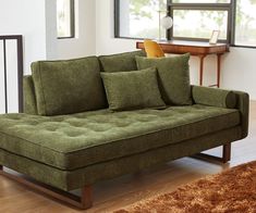 a green couch sitting on top of a hard wood floor next to a wooden table