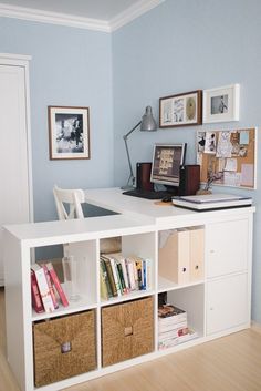 a white desk with baskets and pictures on the wall next to bookshelves in a blue room