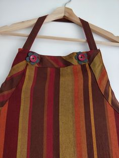 a brown and orange striped bag hanging on a wooden hanger with two flowers in it