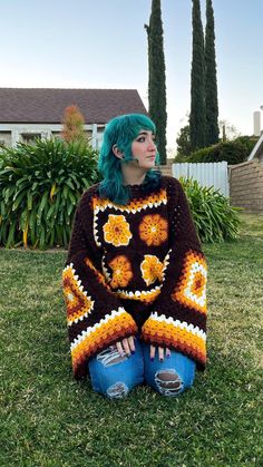 a woman with green hair sitting on the grass in front of her house wearing a crocheted sweater