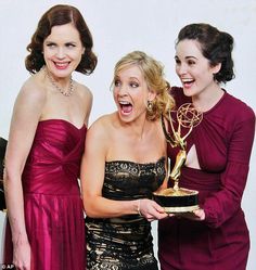 three women in dresses holding an award and posing for the camera with their mouths open