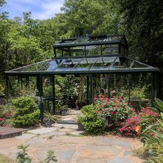 a green house surrounded by trees and flowers