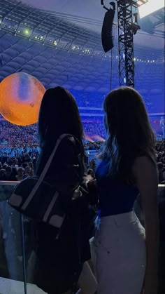 two women are standing in front of an audience at a concert, looking up into the sky