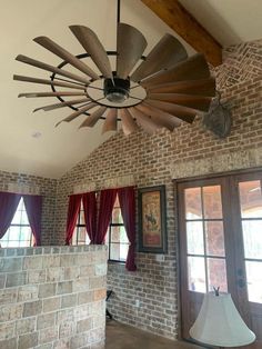 a ceiling fan hanging from the ceiling in a room with brick walls and red curtains