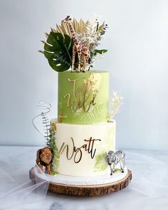 a three tiered cake decorated with jungle animals and greenery on a wooden stand