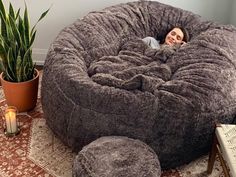 a woman laying in a giant bean bag chair next to a potted snake plant