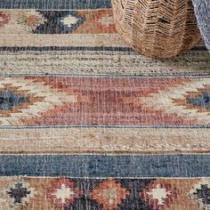 an area rug with various colors and patterns on it, next to a wicker basket