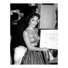 an old black and white photo of a woman in a dress holding up a plaque