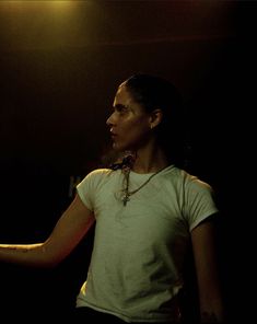 a woman standing in the dark with her hand out and holding something on one arm