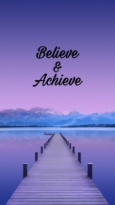 a pier with the words believe and achieve on it in front of mountains, water and sky