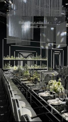 a long table with white flowers and place settings in front of chandelier hanging from the ceiling