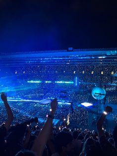 a large crowd at a concert with their hands up in the air and lights on